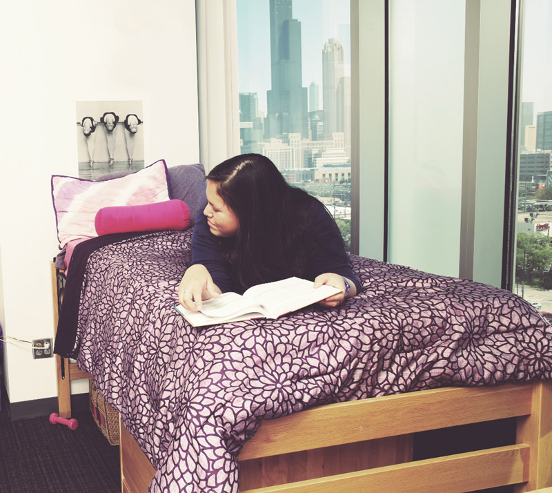 Female student studying on her bed with Chicago Skyline in background